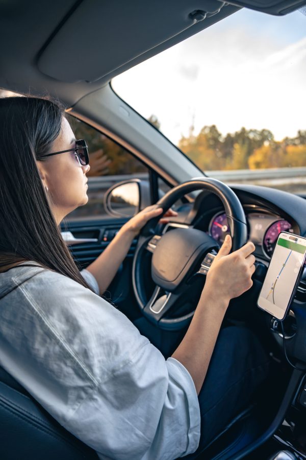 An attractive young woman driving a car uses a navigator in her smartphone.